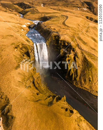 Drone shot of major waterfall in Iceland, with overflow of water falling down from magnificent brown stones. Beautiful scenery formed by amazing icelandic skgafoss cascade pouring over hills. 112031090