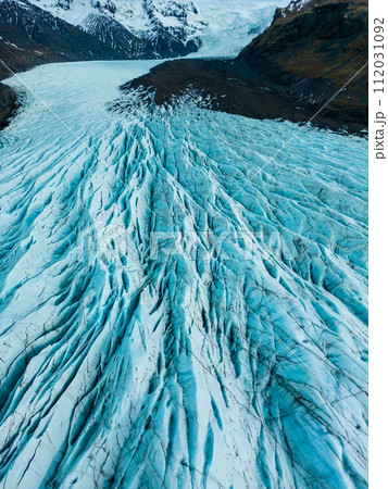 Aerial view of glacier ice cap on wintry region, massive blocks of cracked ice with crevasses in iceland. Spectacular blue diamond shaped rocks creates nordic landscapes, covered frost icebergs. Aerial view of glacier ice cap on wintry region, massive blocks of cracked ice with crevasses in iceland. Spectacular blue diamond shaped rocks creates nordic landscapes, covered frost icebergs. 112031092