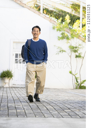リュックを肩にかけて歩く笑顔の50代の男性  リュックを肩にかけて歩く笑顔の50代の男性  112031125
