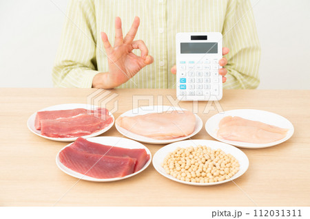 タンパク質の多い食材と電卓を持って丸サインをするミドル女性 112031311