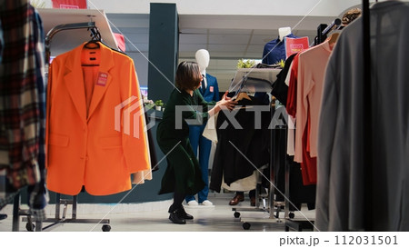 Customer checking fashion items on racks in department store, making purchases at shopping center during black friday promotions. Client buying clothing items from hangers. Handheld shot. 112031501