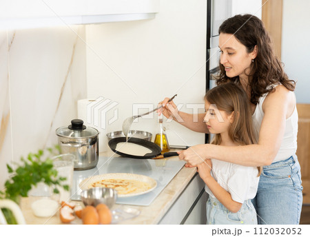 Happy mother and daughter frying pancakes in the kitchen Happy mother and daughter frying pancakes in the kitchen 112032052
