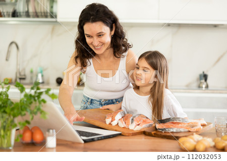 Happy mother and her daughter preparing salmon in the kitchen 112032053