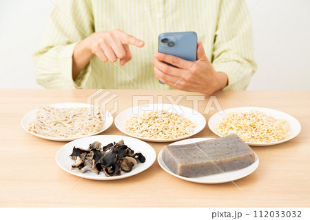 食物繊維を多く含む食品とスマホを操作するミドル女性 112033032