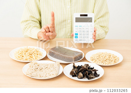 食物繊維を多く含む食品と電卓を持って人差し指を立てるミドル女性 112033265