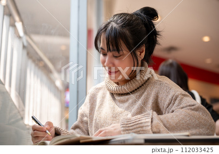 A beautiful Asian woman is keeping her diary or making list of her ideas, working remotely at a cafe 112033425