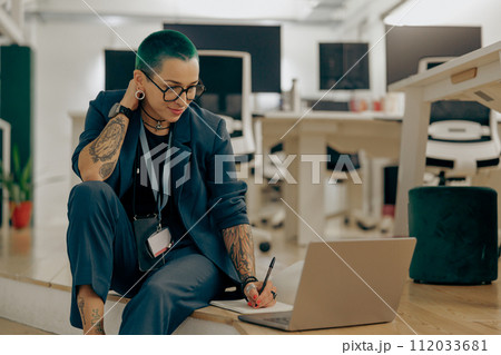 Pretty tattooed business woman with green short hair is use laptop sitting in modern coworking Pretty tattooed business woman with green short hair is use laptop sitting in modern coworking 112033681