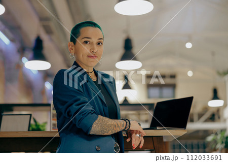 Portrait of creative tattooed female manager with green short hair on modern coworking background Portrait of creative tattooed female manager with green short hair on modern coworking background 112033691