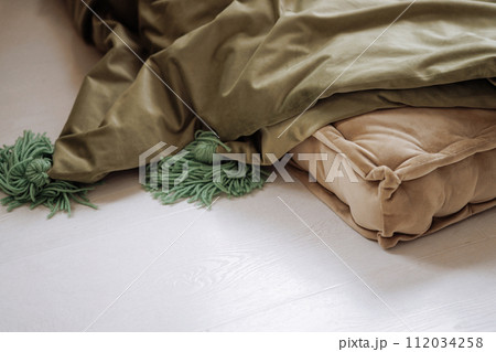 Green and beige blankets lie carelessly on the white floor. Green and beige blankets lie carelessly on the white floor. 112034258