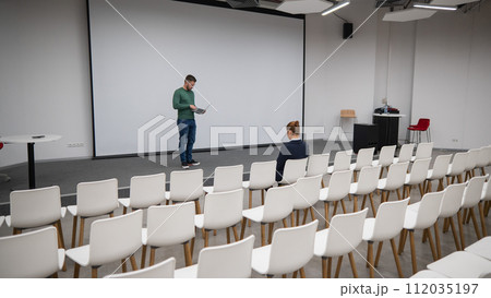 A red-haired Caucasian businesswoman sits in the front row of an empty conference room. Bearded man giving a lecture.  112035197