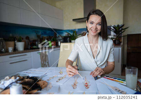 Woman drawing sketches of swimwear and underwear in watercolor while sitting in the kitchen. Woman drawing sketches of swimwear and underwear in watercolor while sitting in the kitchen. 112035241