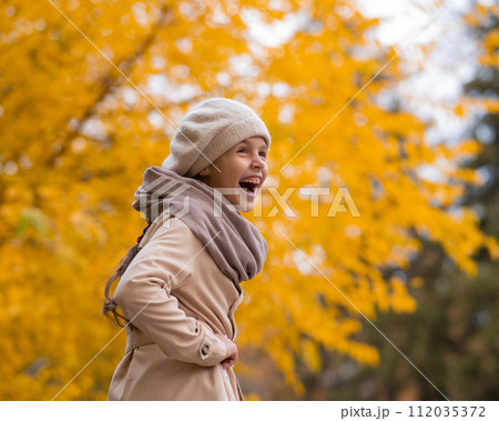 Happy caucasian girl in a beige coat and beret walks in the park in autumn. 112035372