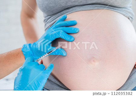 Doctor gives an injection in the stomach of a pregnant woman.  112035382