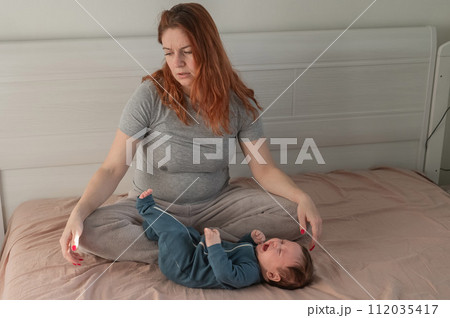A Caucasian woman sits on a bed next to a crying baby. Postpartum depression. 112035417