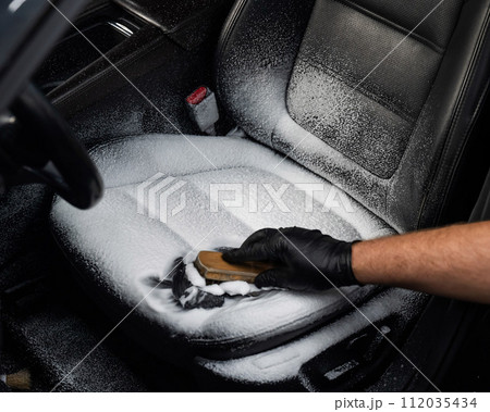 Man cleaning black leather car seat with brush and cleaning foam.  112035434