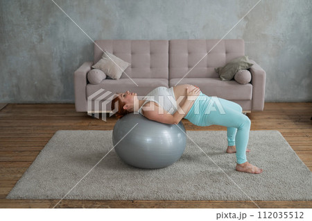 Pregnant red-haired woman doing exercises on fitness ball at home. Pregnant red-haired woman doing exercises on fitness ball at home. 112035512