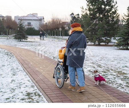 Caucasian woman driving her friend in a wheelchair along the lake in winter. Caucasian woman driving her friend in a wheelchair along the lake in winter. 112035666