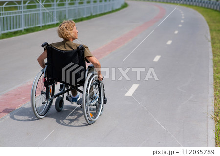 Rear view of an elderly woman in a wheelchair riding on a bike path.  112035789
