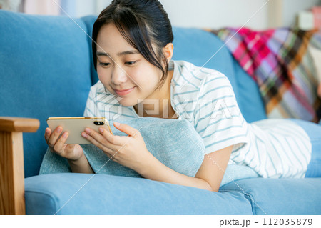 リビングでスマホを見る若い女性 112035879