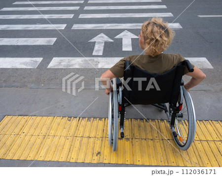 Rear view of an elderly woman on a wheelchair going to a pedestrian crossing.  112036171