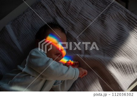 Close-up portrait of a newborn boy with a prism beam on his face. Rainbow. Close-up portrait of a newborn boy with a prism beam on his face. Rainbow. 112036302