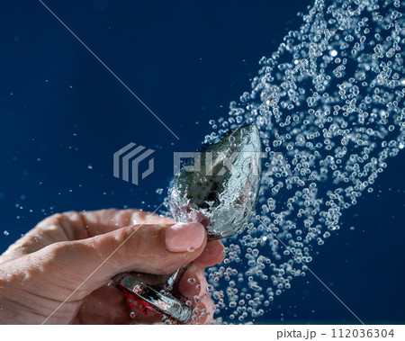 Woman washing silver butt plug under shower on blue background. Woman washing silver butt plug under shower on blue background. 112036304