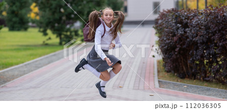 Happy caucasian girl in uniform and with a backpack jumping outdoors after school. Happy caucasian girl in uniform and with a backpack jumping outdoors after school. 112036305