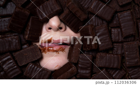 The face of a caucasian woman surrounded by sweets. Girl licks chocolate-stained lips.  112036306