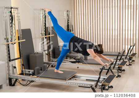 Overweight caucasian woman doing pilates exercises on a reformer. Overweight caucasian woman doing pilates exercises on a reformer. 112036408