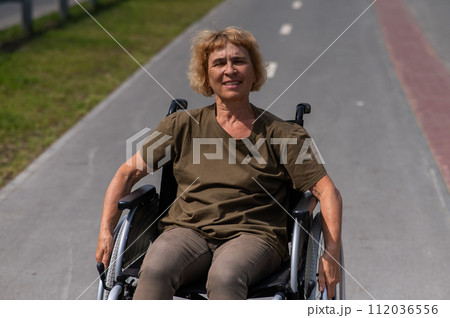 Happy elderly woman on a wheelchair rides along a bike path.  112036556