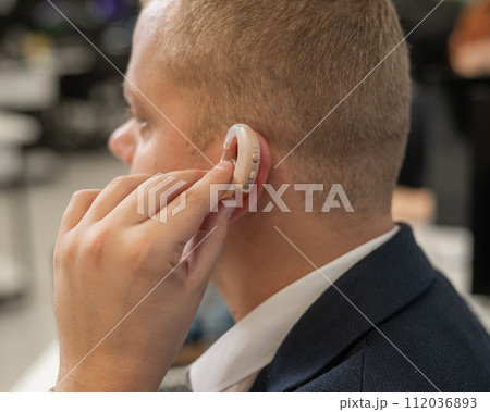 Young caucasian man putting on a hearing aid. Young caucasian man putting on a hearing aid. 112036893
