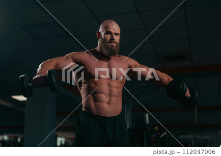 A muscular shirtless man lifts dumbbells to the sides with dumbbells in the gym. 112037006