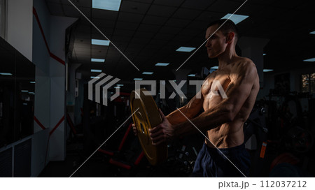 Muscular shirtless man doing exercise with weight plate in gym. Muscular shirtless man doing exercise with weight plate in gym. 112037212