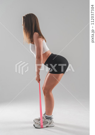 Caucasian woman doing exercises with fitness elastic band on white background. Vertical photo. 112037384