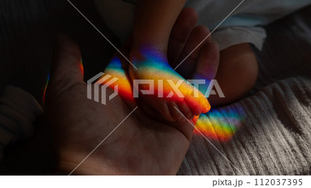 A man holds his newborn son by the leg. Beam of light through a prism.  112037395