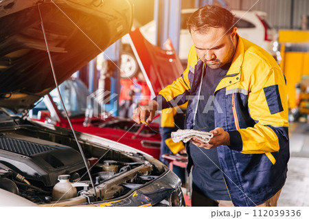 man checking engine oil level in garage. mechanic staff working service car in workshop 112039336