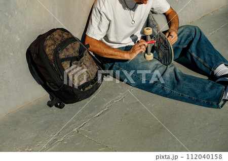 View of a man repairing his skateboard in the skate park. Extreme sport concept View of a man repairing his skateboard in the skate park. Extreme sport concept 112040158