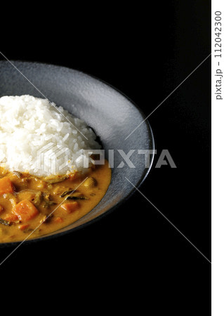 豚肉、かぼちゃ、人参などの野菜が沢山入ったカレーライスを黒背景で撮影 112042300