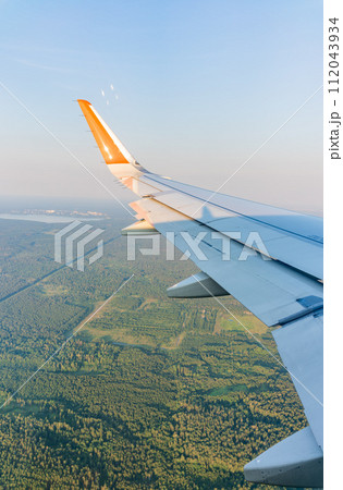 View of airplane wing, blue skies and green land during landing. Airplane window view. View of airplane wing, blue skies and green land during landing. Airplane window view. 112043934