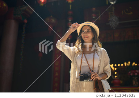 Gorgeous female tourist with camera standing against a Chinese Temple located in Chang Mai Thailand 112045635