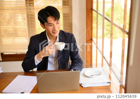 Portrait of handsome businessman drinking coffee and looking through window Portrait of handsome businessman drinking coffee and looking through window 112045639