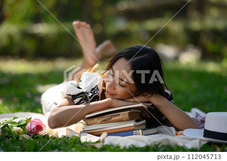 Beautiful young woman falling asleep on a stack of books, enjoys nature and warm weather 112045713