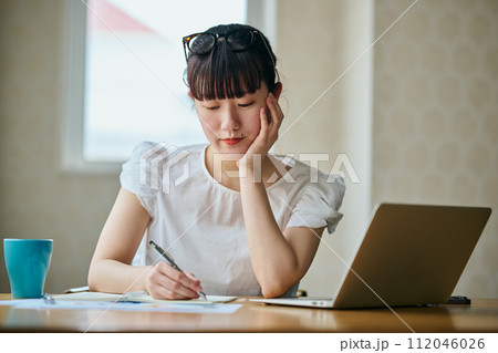 頬杖をつきながらノートにメモをとる若い女性 112046026