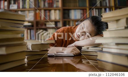 Tired asian student sleeping on stack of book, taking a break from studying 112046106