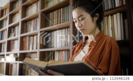 Attractive asian woman librarian flipping through pages of large book at library 112046126
