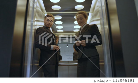 Elevator door opening, embarrassed couple of colleagues exiting, caught flirting 112046191