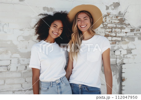 two friends in white t-shirts and jeans, one of them with a hat two friends in white t-shirts and jeans, one of them with a hat 112047950