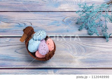 Colorful Easter eggs in a wicker basket on the wooden background 112048990