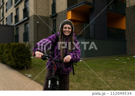 Cute young woman with piercing and dreadlocks riding a bicycle in an urban environment 112049534