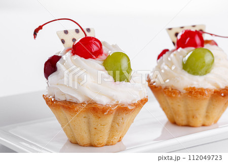 Beautiful cream cakes with cherries and grapes on a plate on a white background Beautiful cream cakes with cherries and grapes on a plate on a white background 112049723